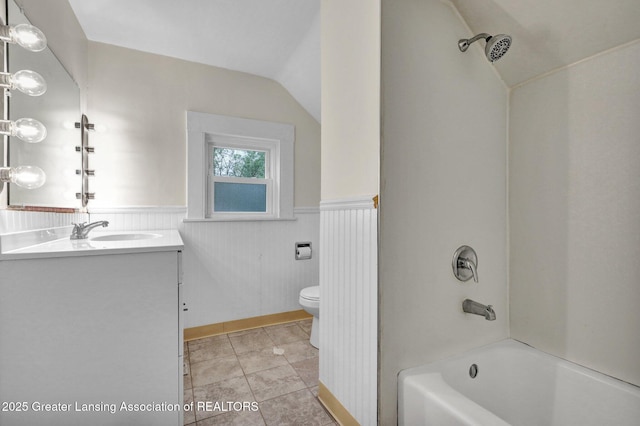 bathroom with toilet, lofted ceiling, vanity, wainscoting, and washtub / shower combination