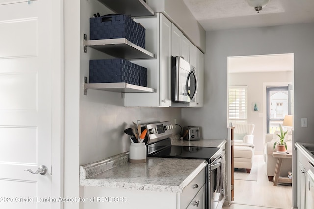 kitchen with stainless steel appliances, open shelves, white cabinetry, and light countertops