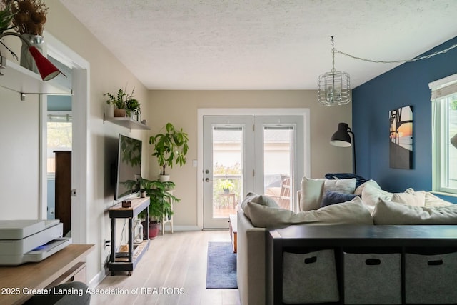 living area with light wood-style flooring, a chandelier, a textured ceiling, and baseboards