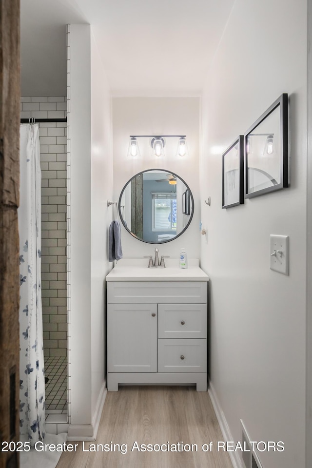 bathroom featuring wood finished floors, a shower stall, baseboards, and vanity