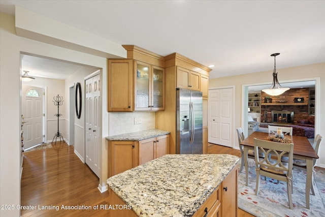 kitchen featuring stainless steel fridge, light wood-type flooring, glass insert cabinets, light stone counters, and decorative backsplash
