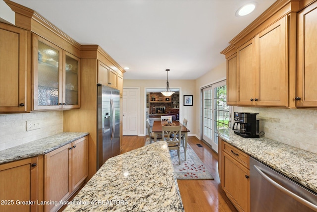 kitchen featuring appliances with stainless steel finishes, wood finished floors, glass insert cabinets, tasteful backsplash, and recessed lighting