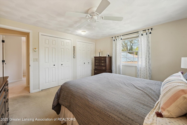bedroom featuring light colored carpet, two closets, baseboards, and ceiling fan
