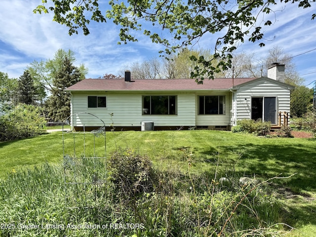 back of property with a chimney, a lawn, and central AC unit