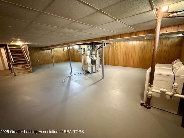 finished below grade area featuring washer and dryer, wooden walls, stairway, heating unit, and a drop ceiling