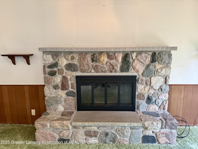 detailed view of a wainscoted wall, a stone fireplace, wooden walls, and carpet floors
