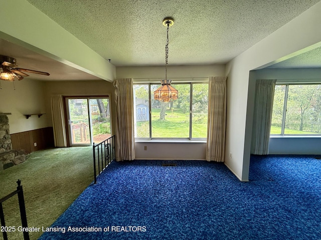 unfurnished dining area with carpet flooring, ceiling fan, wainscoting, a textured ceiling, and a chandelier