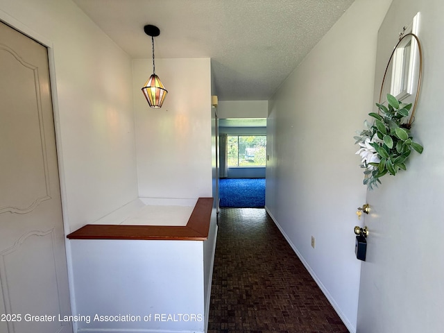 hall featuring baseboards, brick patterned floors, and a textured ceiling
