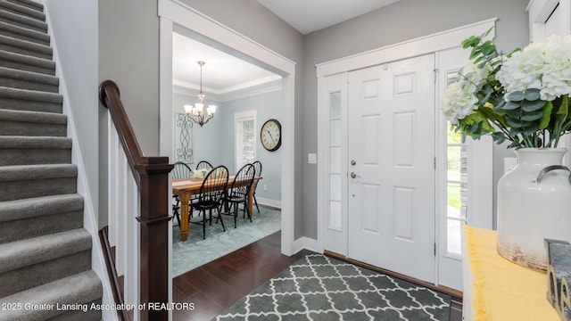 foyer entrance with stairway, a chandelier, dark wood finished floors, baseboards, and crown molding