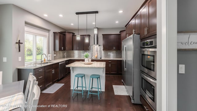 kitchen with appliances with stainless steel finishes, wall chimney range hood, a center island, dark brown cabinetry, and a sink