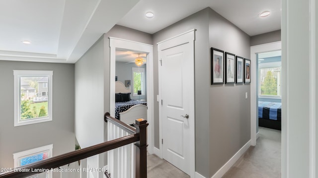 corridor with an upstairs landing, light carpet, and baseboards