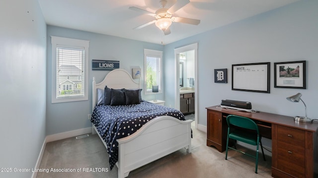 carpeted bedroom featuring baseboards, ensuite bath, a desk, and a ceiling fan
