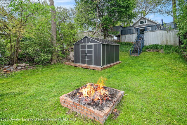 15496 Park Lake Rd, East Lansing, MI 48823 - view of green lawn featuring an outdoor fire pit, stairs, a storage shed, a wooden deck, and an outdoor structure