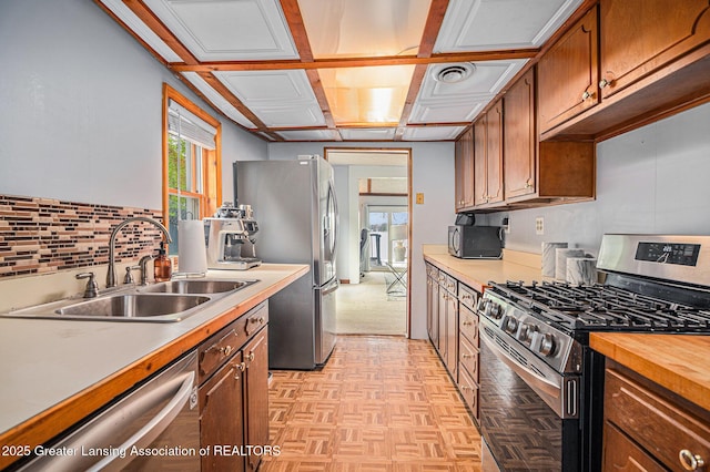 15496 Park Lake Rd, East Lansing, MI 48823 - kitchen with appliances with stainless steel finishes, a sink, decorative backsplash, brown cabinetry, and wooden counters