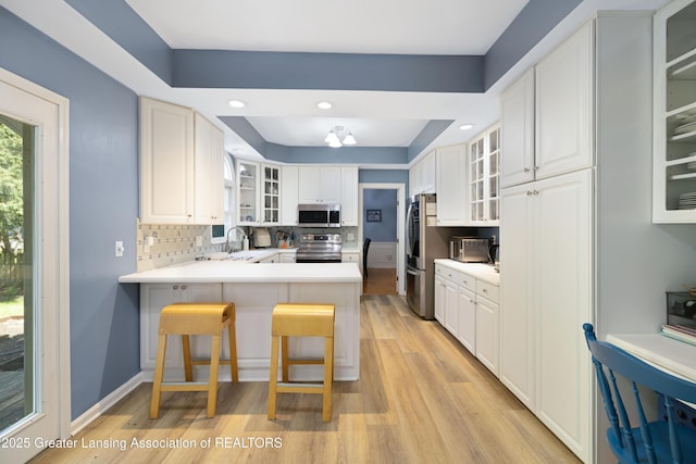 2038 Woodfield Rd, Okemos, MI 48864 - kitchen featuring stainless steel appliances, light wood finished floors, a peninsula, a tray ceiling, and glass insert cabinets