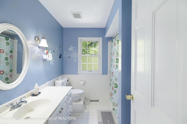 2038 Woodfield Rd, Okemos, MI 48864 - bathroom featuring tile patterned floors, toilet, tile walls, a wainscoted wall, and vanity
