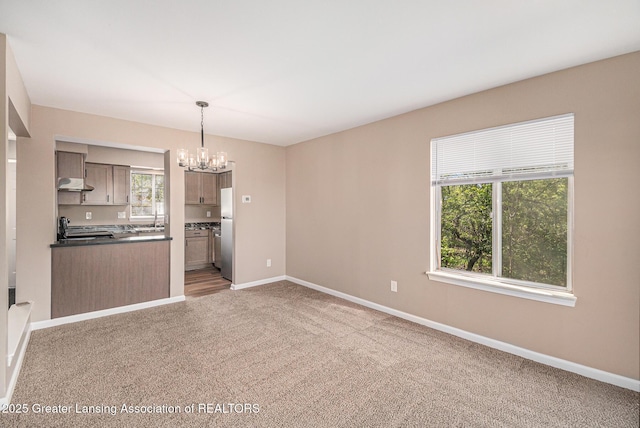 1626 Pepper Tree Ln Unit 13, Lansing, MI 48912 - kitchen featuring freestanding refrigerator, a chandelier, under cabinet range hood, dark countertops, and carpet floors