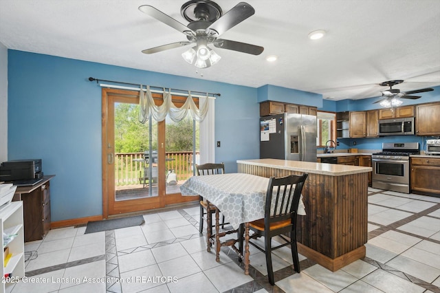 kitchen with appliances with stainless steel finishes, a ceiling fan, inlaid floor details, and light tile patterned flooring