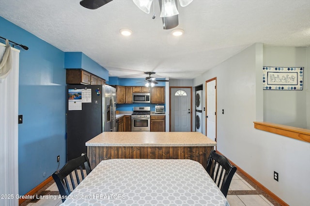 kitchen featuring a ceiling fan, appliances with stainless steel finishes, stacked washing machine and dryer, baseboards, and light countertops