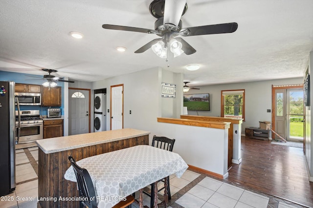 kitchen featuring appliances with stainless steel finishes, stacked washer and clothes dryer, ceiling fan, baseboards, and light countertops