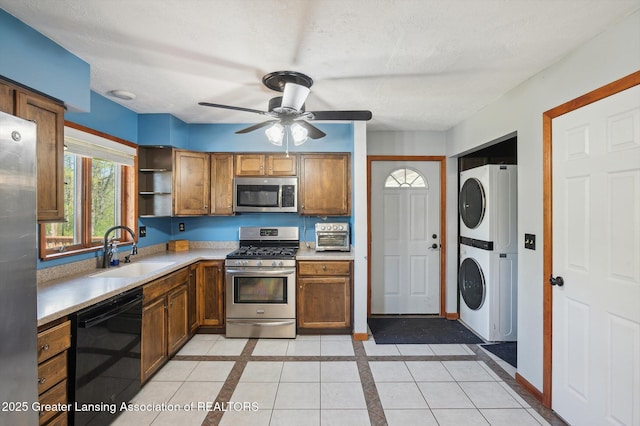 kitchen featuring appliances with stainless steel finishes, stacked washer / drying machine, a sink, a ceiling fan, and light countertops