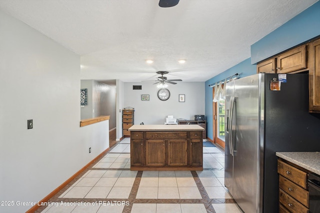 kitchen featuring stainless steel fridge with ice dispenser, a ceiling fan, light tile patterned floors, a center island, and baseboards