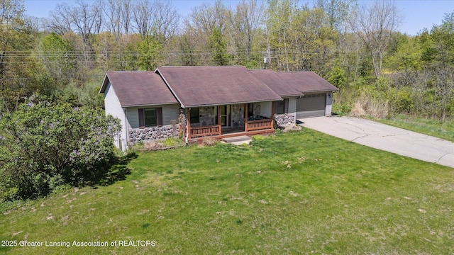 ranch-style home featuring a porch, an attached garage, concrete driveway, a forest view, and a front yard