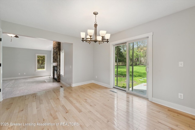 263 E Sherwood Rd, Williamston, MI 48895 - unfurnished room featuring light wood-style floors, a chandelier, baseboards, and a stone fireplace