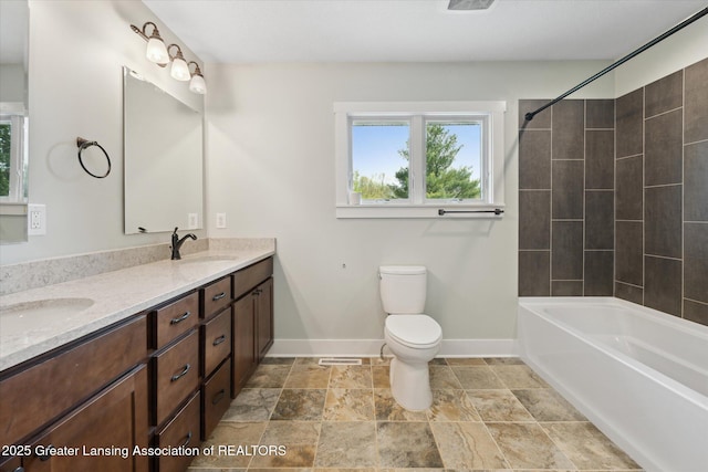 263 E Sherwood Rd, Williamston, MI 48895 - bathroom featuring baseboards, toilet, double vanity, stone finish floors, and bathtub / shower combination