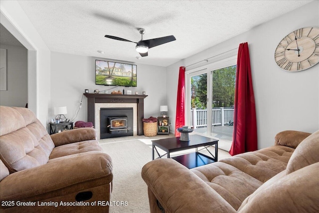living area with carpet floors, a textured ceiling, ceiling fan, and a warm lit fireplace