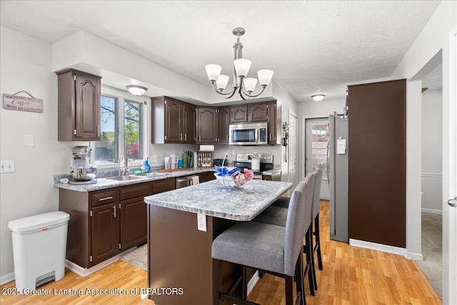 kitchen with appliances with stainless steel finishes, a sink, dark brown cabinetry, light countertops, and a textured ceiling