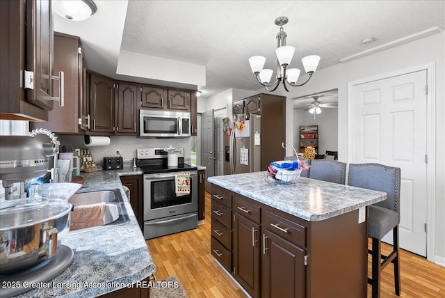 kitchen with appliances with stainless steel finishes, dark brown cabinetry, a kitchen breakfast bar, a chandelier, and a textured ceiling
