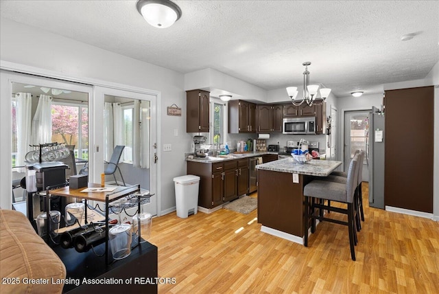 kitchen with appliances with stainless steel finishes, dark brown cabinets, light countertops, light wood finished floors, and a textured ceiling