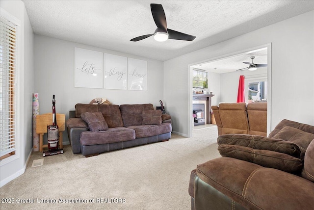 living area with ceiling fan, carpet flooring, a textured ceiling, a fireplace, and baseboards