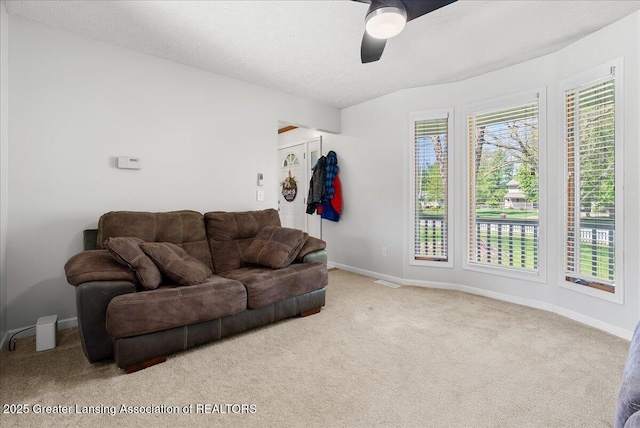 living area with ceiling fan, carpet, baseboards, and a textured ceiling