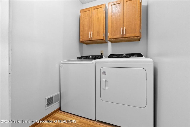 clothes washing area featuring cabinet space, separate washer and dryer, and light wood-style floors