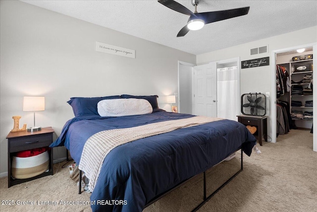 bedroom featuring carpet, a spacious closet, a textured ceiling, a closet, and ceiling fan