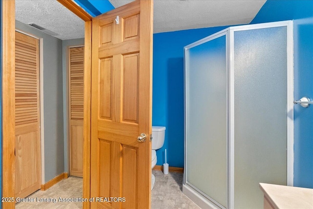 bathroom with a textured ceiling, a shower stall, toilet, a closet, and baseboards