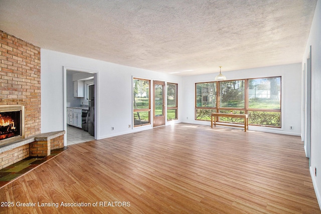 160 Lincoln Hill Dr, Battle Creek, MI 49015 - unfurnished living room featuring light wood finished floors, a fireplace, a textured ceiling, plenty of natural light, and baseboards