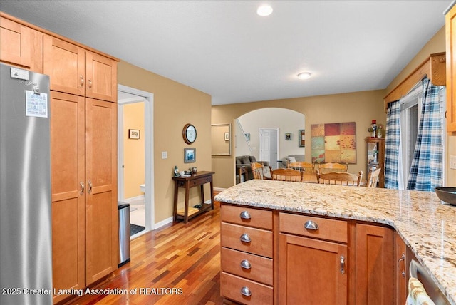13503 Cottonwood Ct, Dewitt, MI 48820 - kitchen with freestanding refrigerator, a peninsula, light wood-style flooring, arched walkways, and light stone countertops