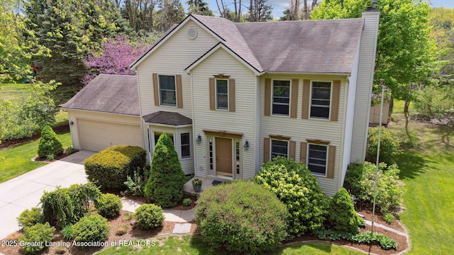 view of front facade with an attached garage, driveway, a chimney, a front lawn, and a shingled roof