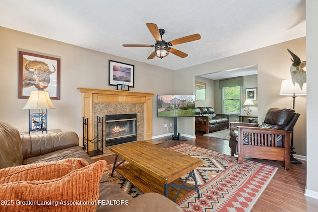 living area featuring wood finished floors, a ceiling fan, a fireplace, and baseboards