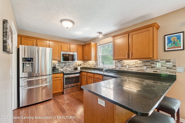 kitchen with appliances with stainless steel finishes, a sink, a peninsula, dark countertops, and a textured ceiling