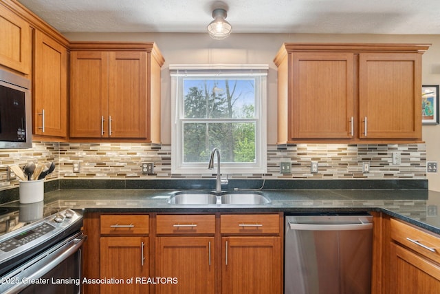 kitchen featuring stainless steel appliances, a sink, decorative backsplash, dark stone countertops, and brown cabinetry