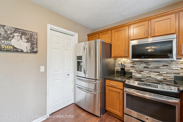 kitchen featuring appliances with stainless steel finishes, dark wood-style floors, backsplash, dark countertops, and brown cabinets