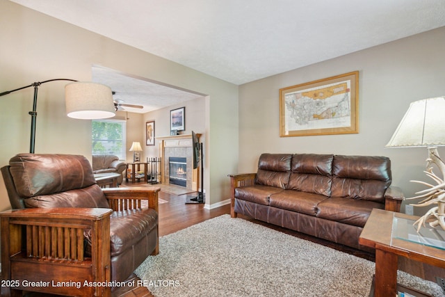 living area with wood finished floors, ceiling fan, baseboards, and a tiled fireplace