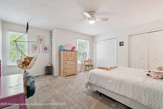 bedroom featuring multiple closets, carpet floors, multiple windows, ceiling fan, and a textured ceiling