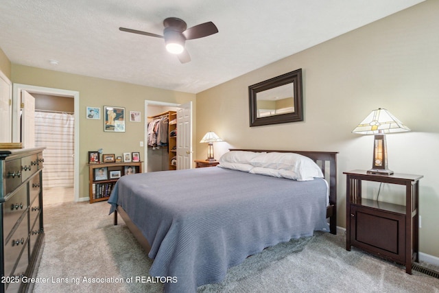 bedroom with a walk in closet, light carpet, a closet, ensuite bathroom, and baseboards