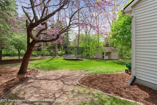 view of green lawn with a trampoline, an outbuilding, and view of wooded area