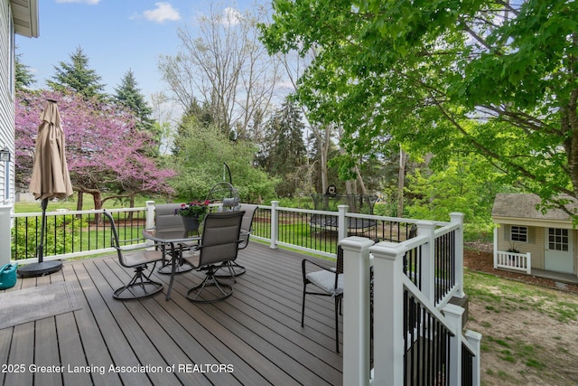deck featuring outdoor dining space, an outbuilding, and view of wooded area